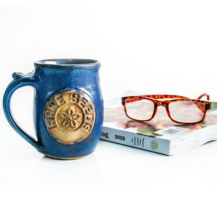 A Handmade Local Mug Blue/Grey Pottery with a Whole Seed Catalog and reading glasses.
