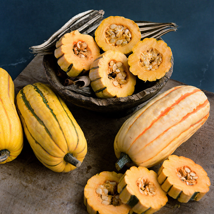 Whole and sliced Delicata Winter Squash on wooden cutting board against a jade background.