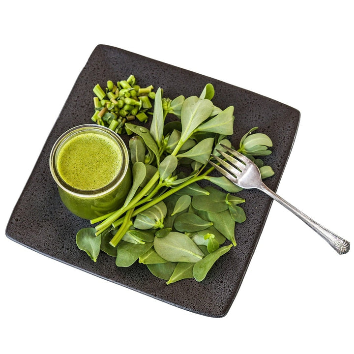 Green Purslane leaves on a black plate with green juice on a white background.