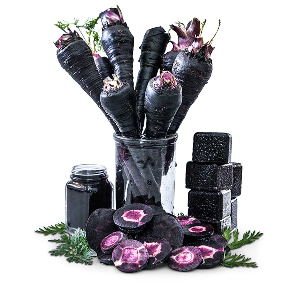 Whole carrots in a glass jar with sliced carrots and greenery surround