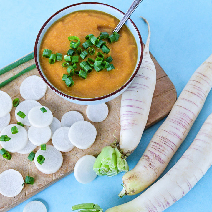 Akasuji Radishes with a bowl of butternut squash soup with radishes on a cutting board on a blue background.