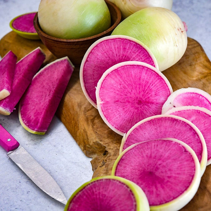Sliced Chinese Red Meat Radishes on wooden cutting board with a pink knife.