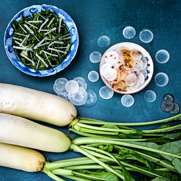 China Jade Radish with cooked radish greens and radish slices in a bowl on teal background.