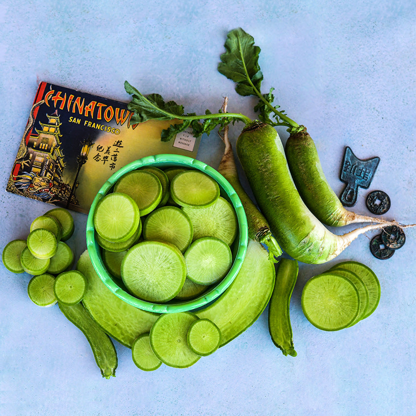Whole and sliced Chinese Shawo Fruit Radish with a post card and coins on light blue background.