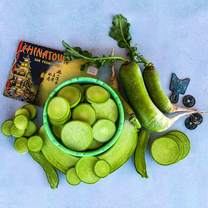 Whole and sliced Chinese Shawo Fruit Radish with a post card and coins on light blue background.