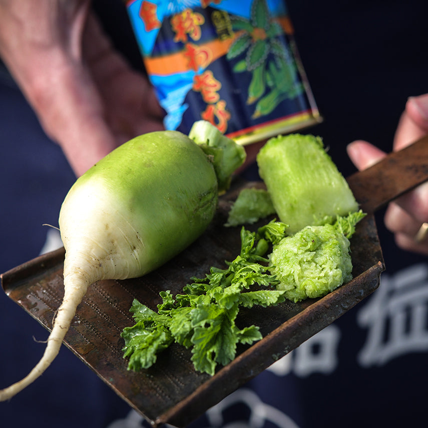 Hands holding grated and whole Japanese Wasabi Radishes with a can of wasabi in the background.