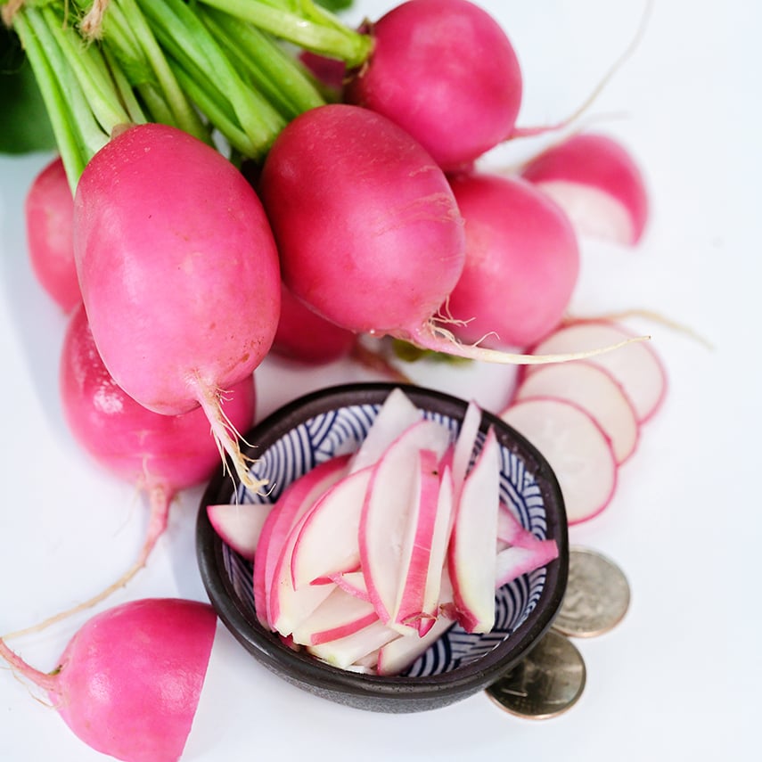 Whole and sliced Pink Dawn Radishes with coins on a white background.