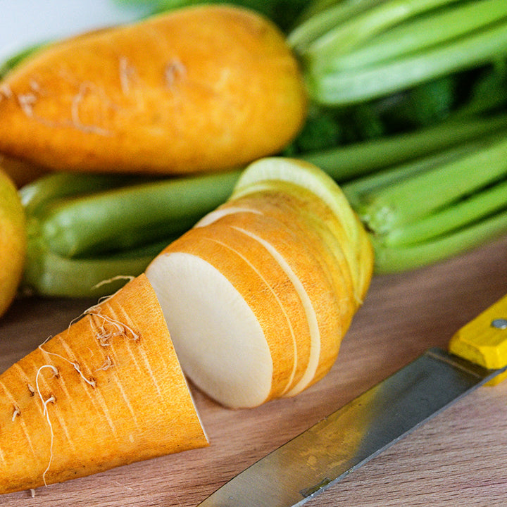 A close-up view of a sliced Lutea Carrot Radish on a cutting board with a knife.