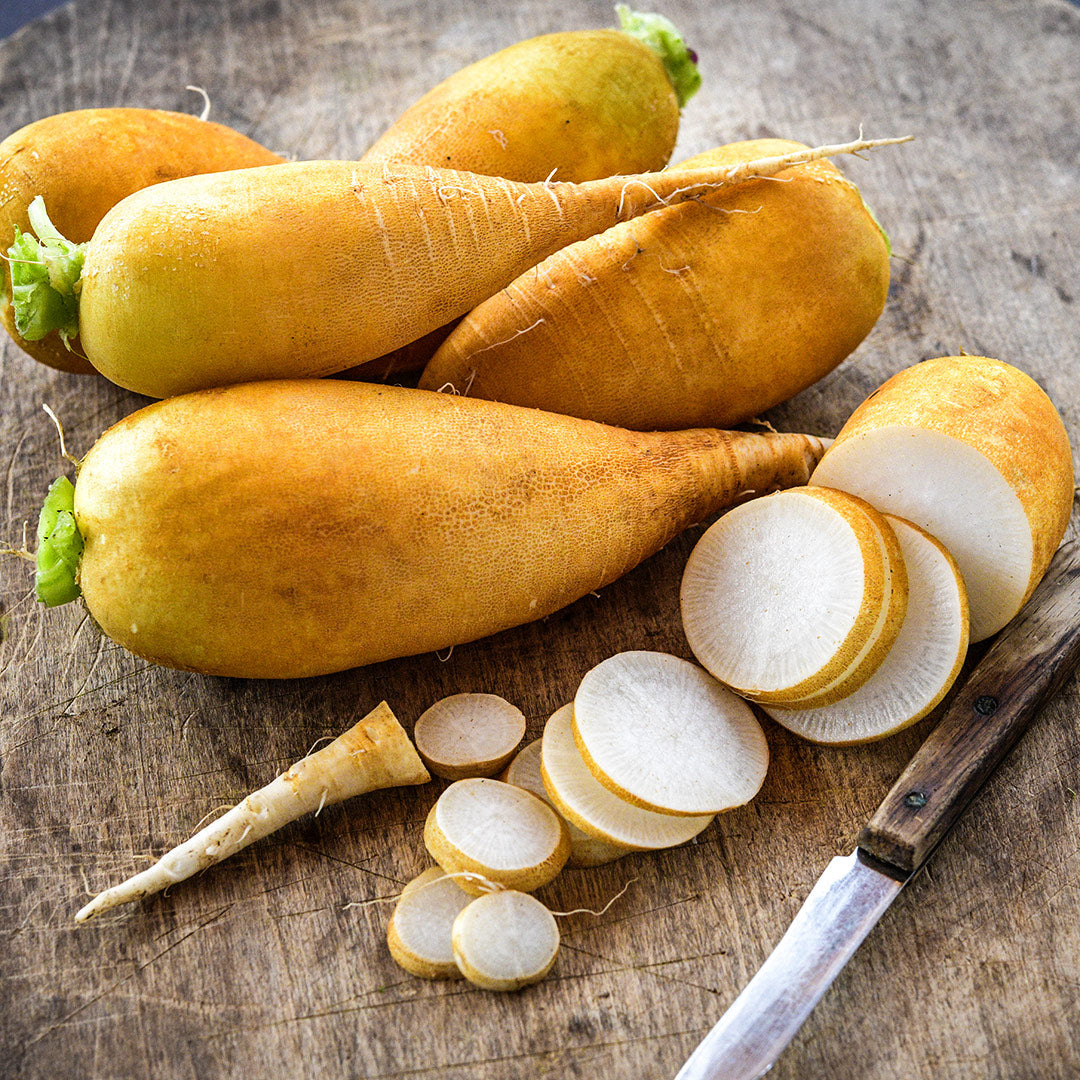 Whole and sliced Lutea Carrot Radishes on a wooden board with a wooden handled knife.