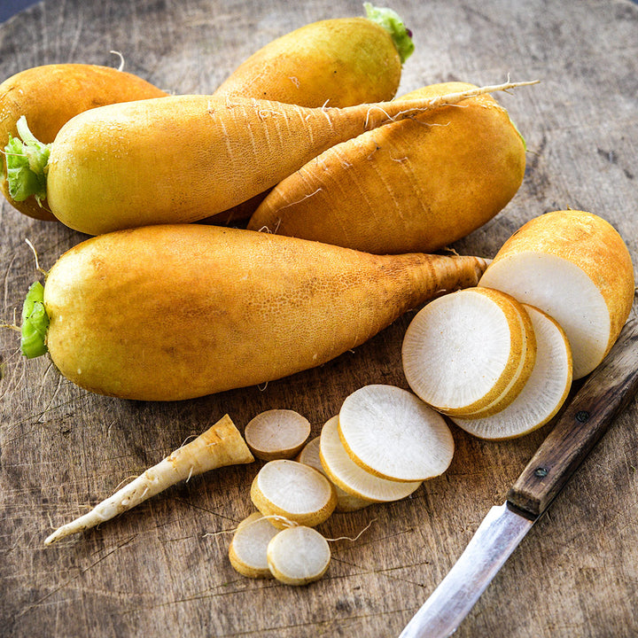 Whole and sliced Lutea Carrot Radishes on a wooden board with a wooden handled knife.