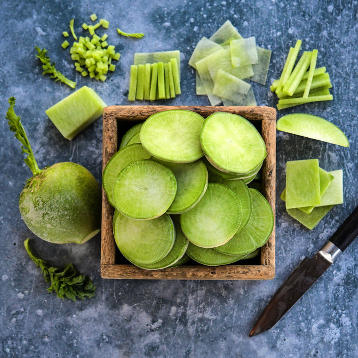 Cut and whole Japanese Wasabi Radishes in a wooden box with a Japanese knife on cement.