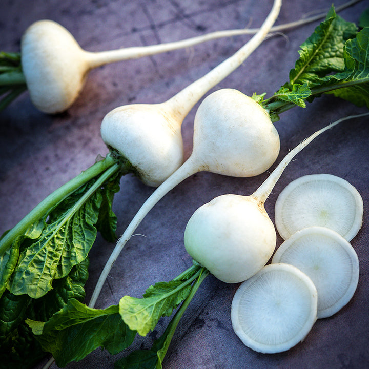 Whole and sliced White Hailstone Radishes on a brown background.