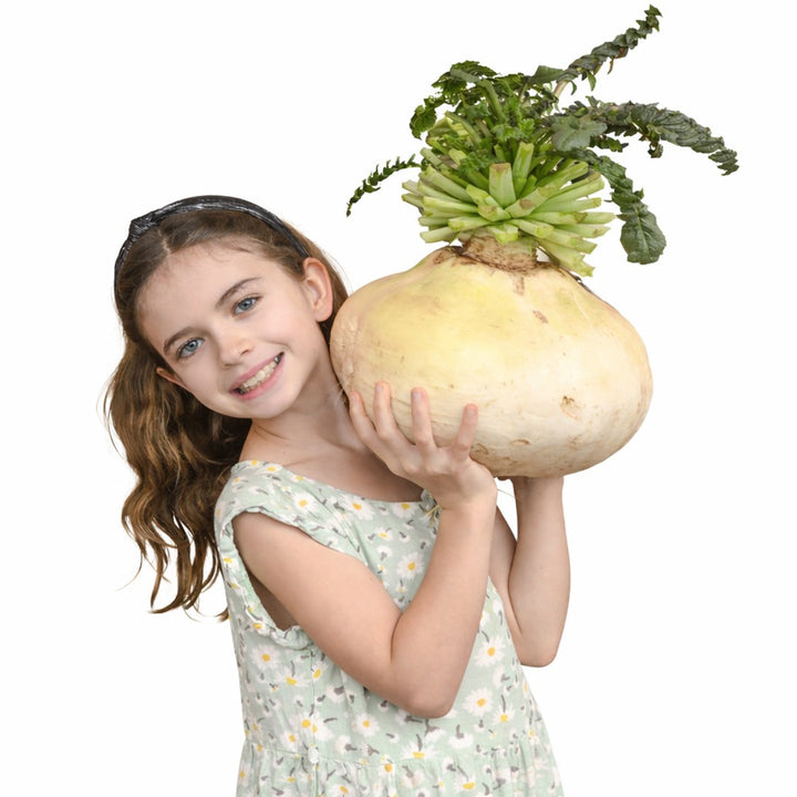 A little girl smiles as she holds a Sakurajima Giant Radish against a white background.
