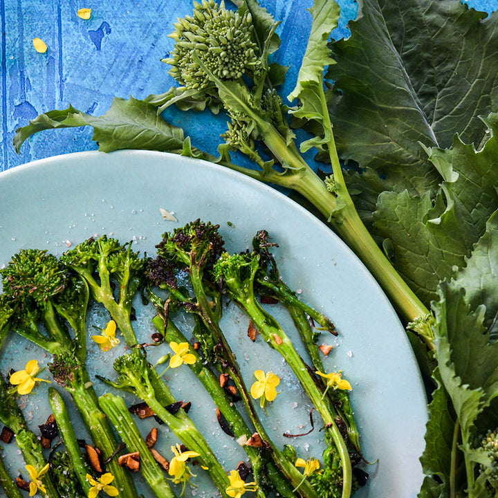 A close-up of seared Natalina Di Fasano Cima Grande Broccoli Rabe on a plate with fresh blooms.