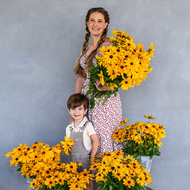 Emilee and Levi Gettle standing with giant bouquets of Viviani Rudbeckia against a grey wall.