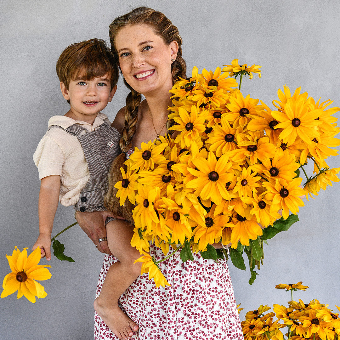 Levi and Emilee Gettle are smiling big while holding a giant bouquet of Viviani Rudbeckia.