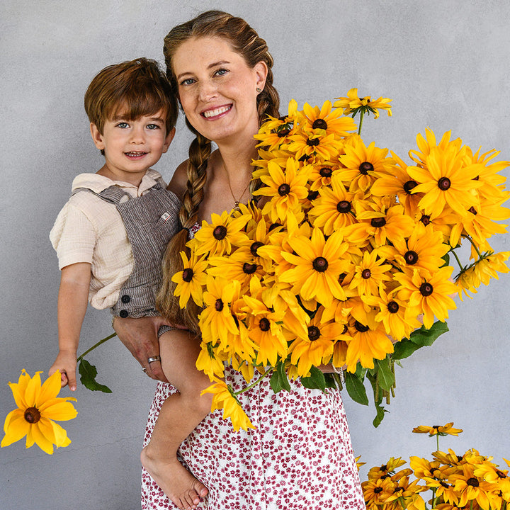 Levi and Emilee Gettle are smiling big while holding a giant bouquet of Viviani Rudbeckia.