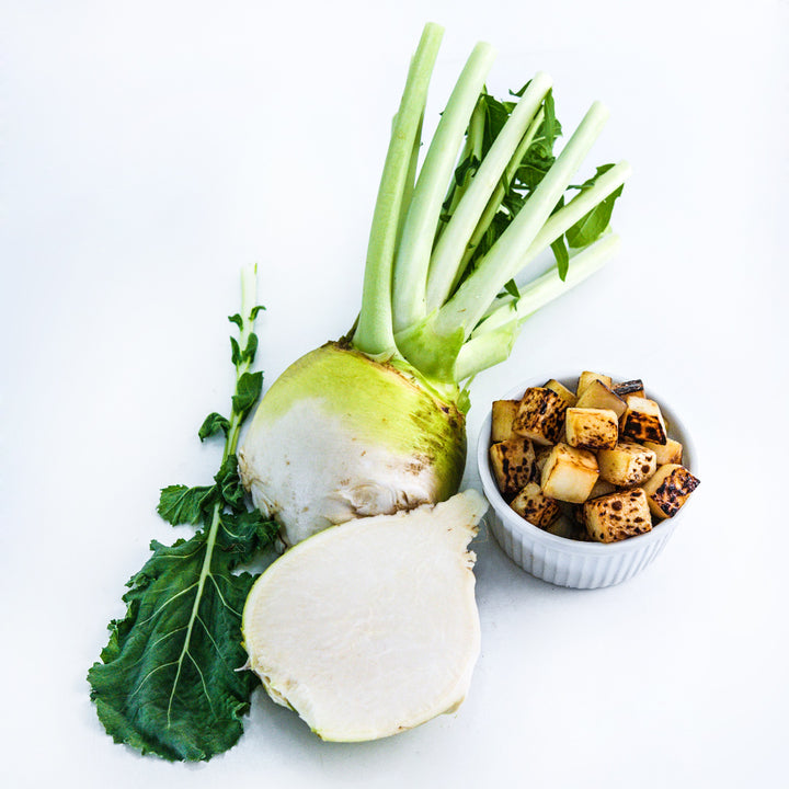 A whole and sliced Macomber Turnip Rutabaga with a bowl full of roasted rutabaga on white.