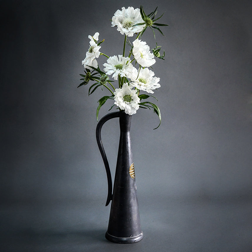 A half dozen Fama White Scabiosa blooms in a tall vase on a grey background.