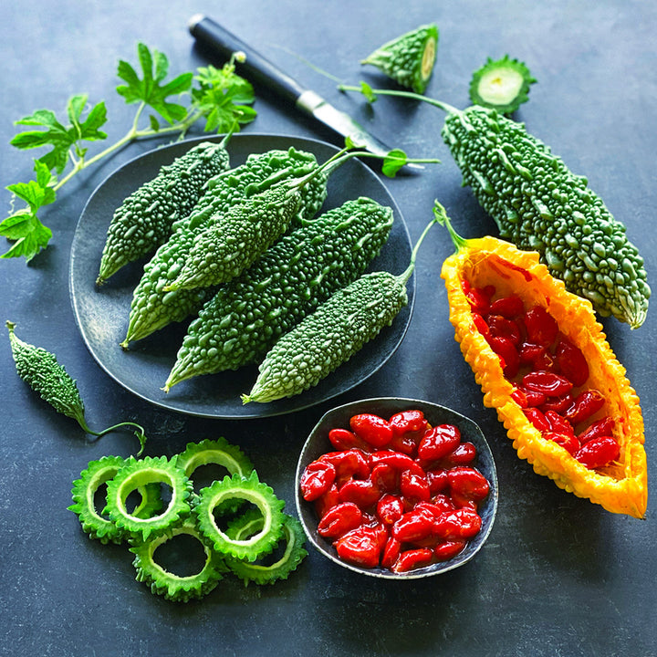 Cut and whole Abashi Bitter Melon with seeds on a jade background.