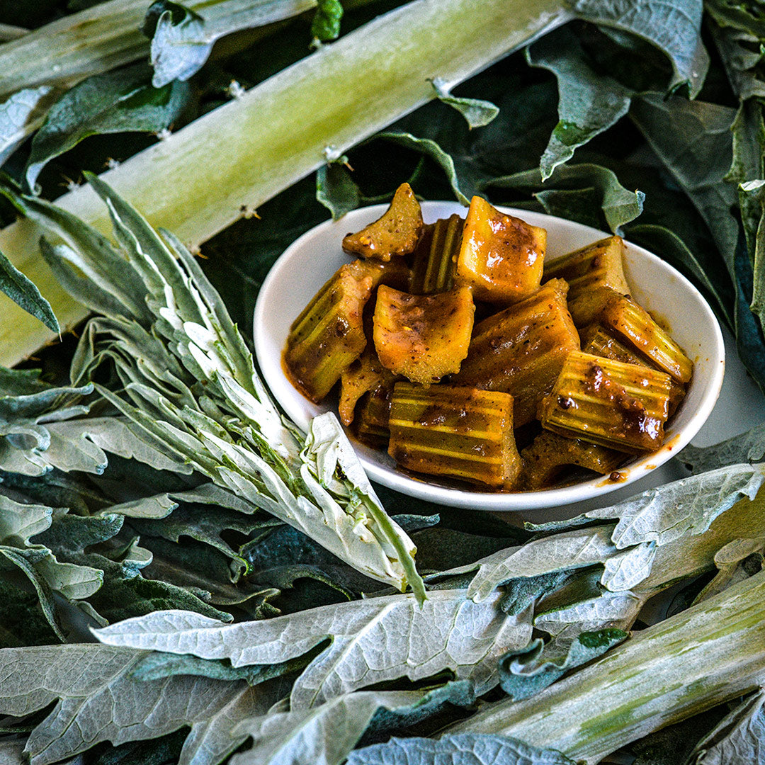 Cooked Gobbo Di Nizzia Cardoon in a bowl surrounded by raw leaves and stems.