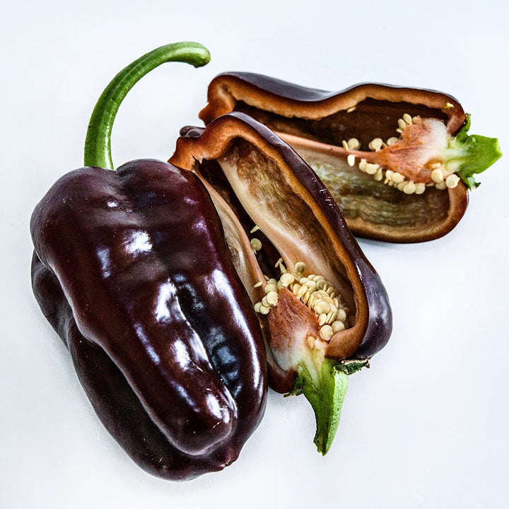 A close-up of cut and whole Sweet Chocolate Sweet Peppers on a white background.