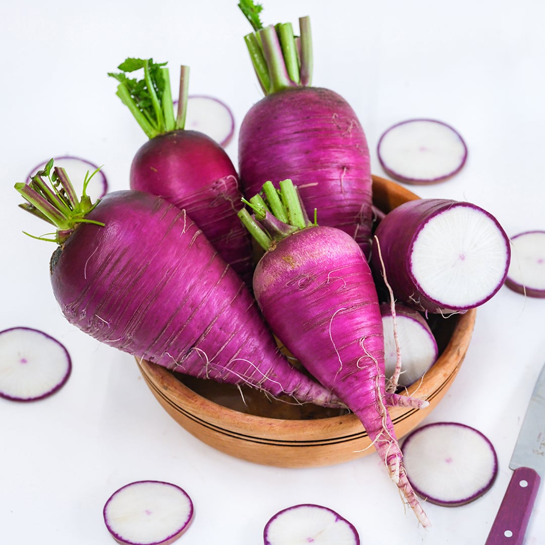 Cut and whole Blue Autumn Radishes surrounded by slices on white background.