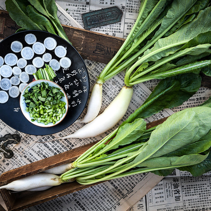 China Jade Radishes in wooden boxes with a salad bowl of greens on top of Chinese newspapers.