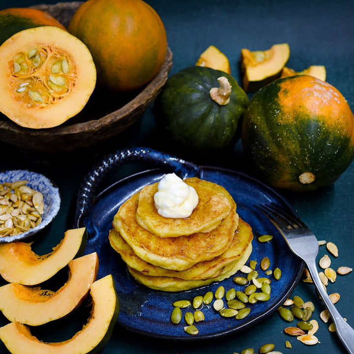 Cut and whole Sweetnut Winter Squash with squash pancakes and seeds on a dark blue background.