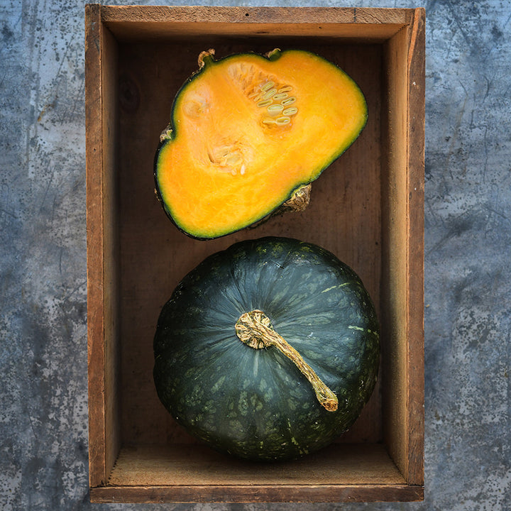 One cut and one whole Buttercup Winter Squash in wooden box on metal background.