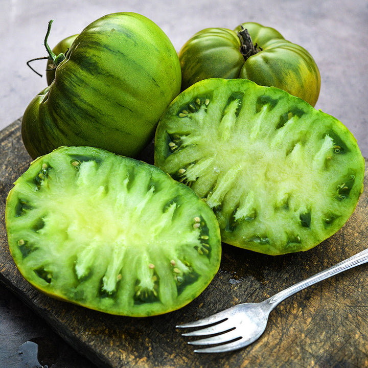 A close-up of cut and whole Spear's Tennessee Green Tomatoes on a wooden cutting board with a fork.
