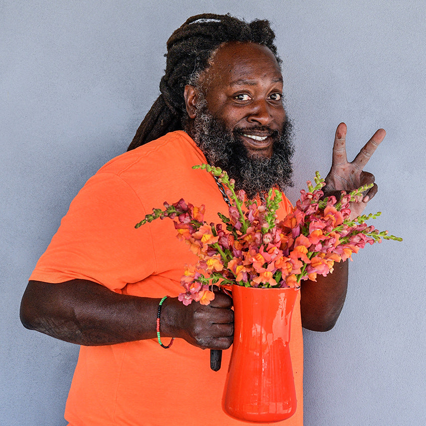 A smiling Baker Creek horticulturalist wearing an orange shirt holding an pitcher full of Orange Wonder Snapdragons.