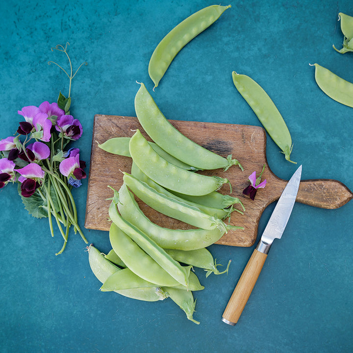 Green Beauty Snow Pea with blooms on cutting board and blue background.
