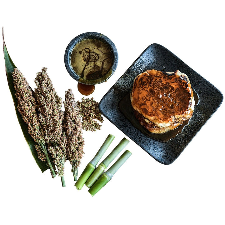 Mennonite Sorghum seed heads and canes with pancakes and sorghum syrup on a white background.