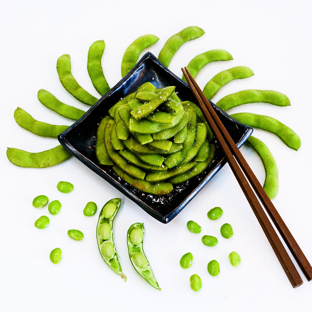 Midori Star Soybean edamame arranged artistically on a black plate surrounded by beans and pods.