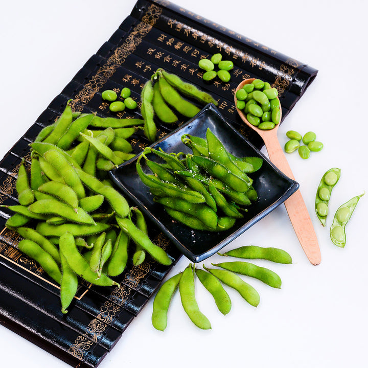 Steamed Chiba Green Soybeans on a plate surrounded by raw and shelled beans on a white background.