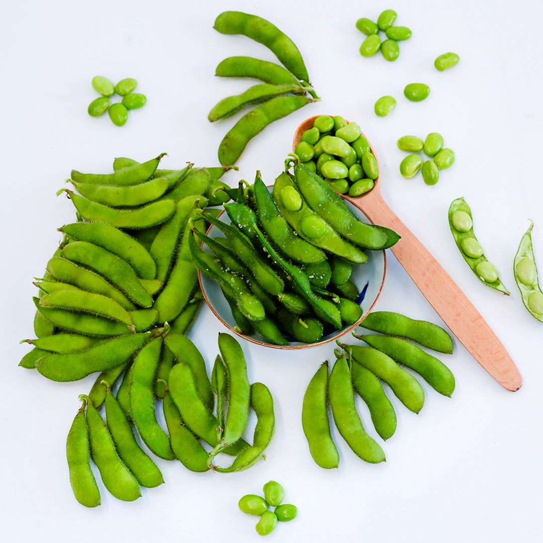 A bowl of steamed Chiba Green Soybeans surrounded by pods and beans on a white background.