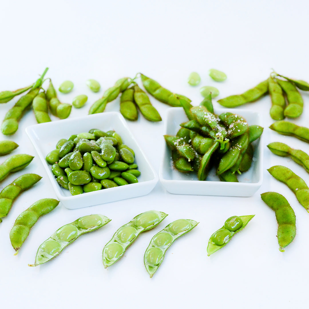 Cooked Tankuro Soybeans in a couple small dishes surrounded by more soybeans on a white background.