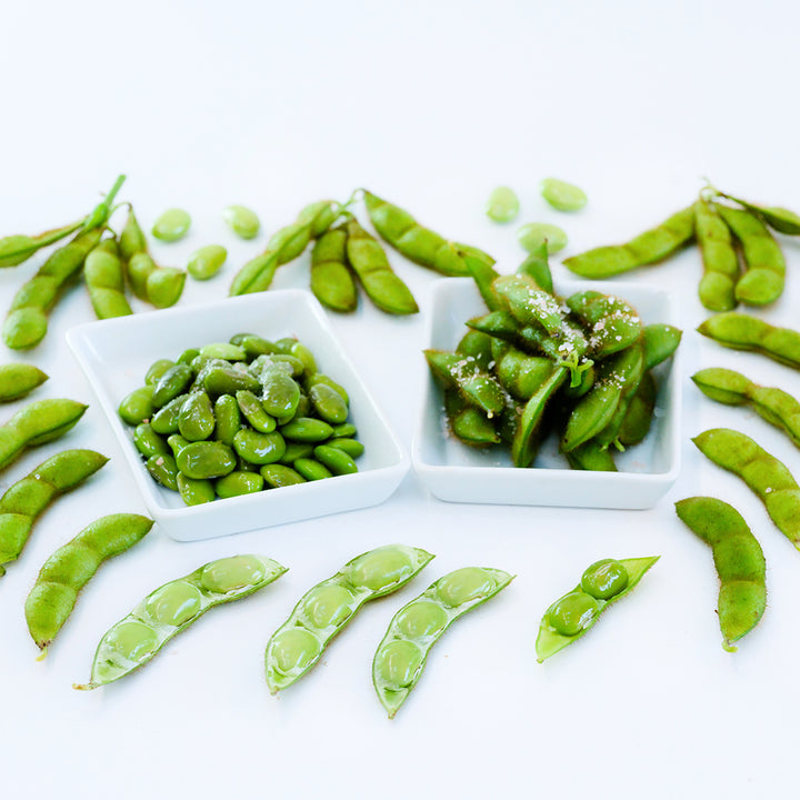 Cooked Tankuro Soybeans in a couple small dishes surrounded by more soybeans on a white background.