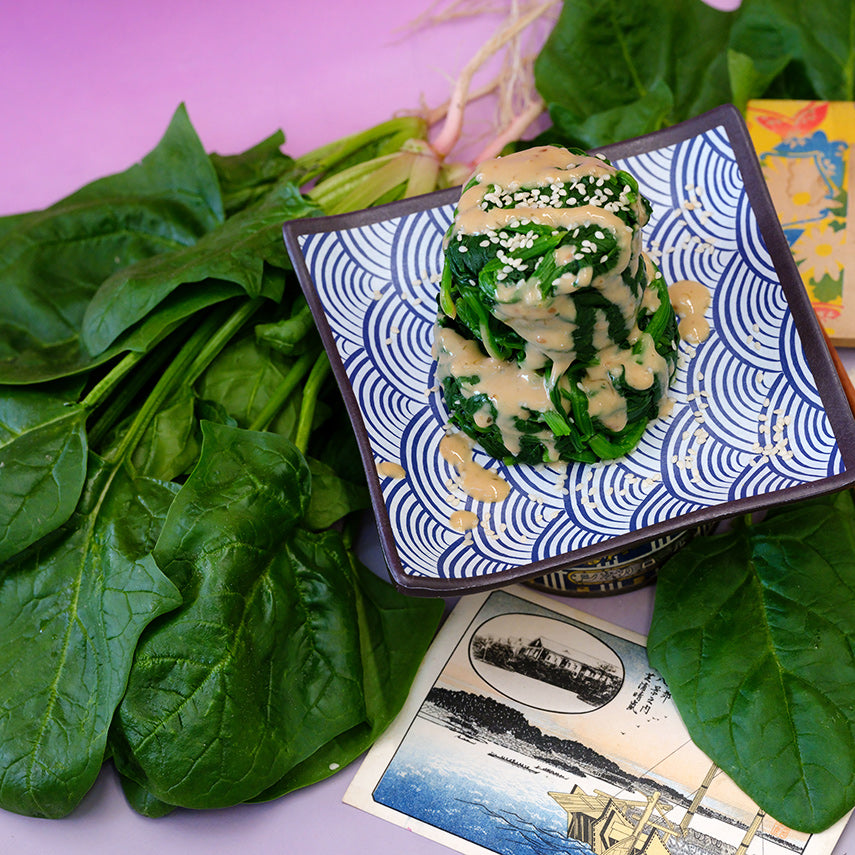 Steamed Jiromaru Spinach on a plate with some fresh leaves on pink background.