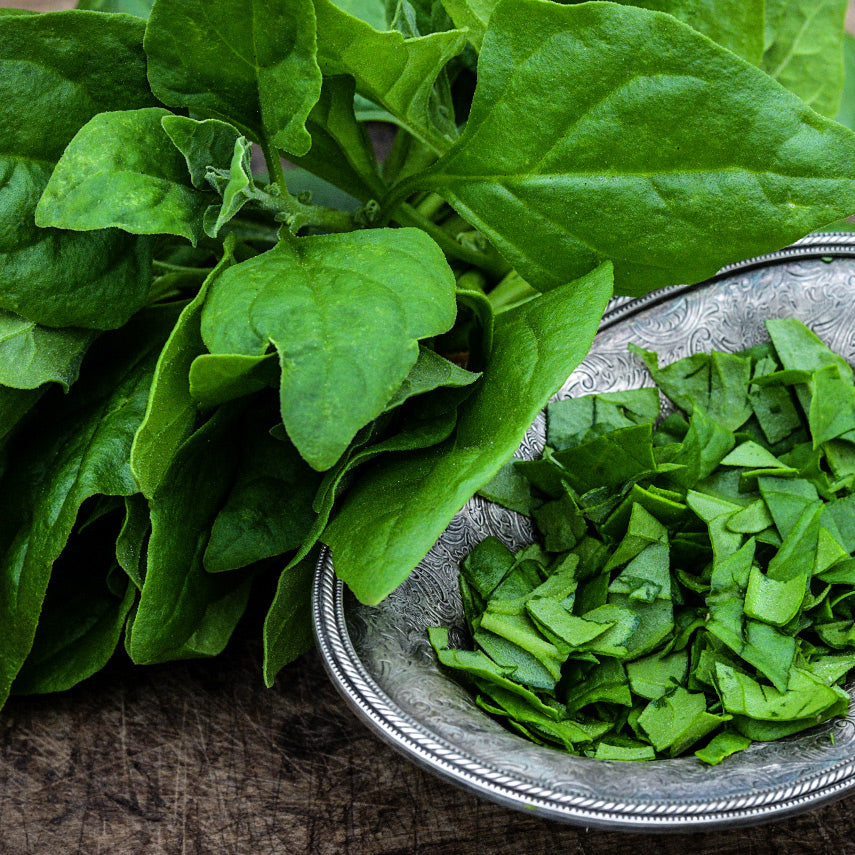 Close-up of New Zealand Spinach leaves and cut spinach in a silver bowl on wood background.