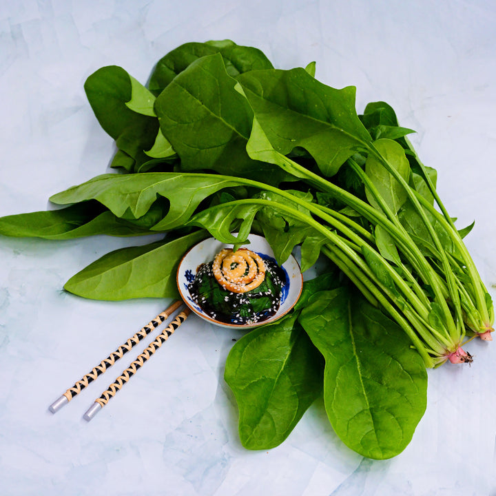 Jiromaru Spinach leaves with some cooked in bowl with chopsticks on light green background.