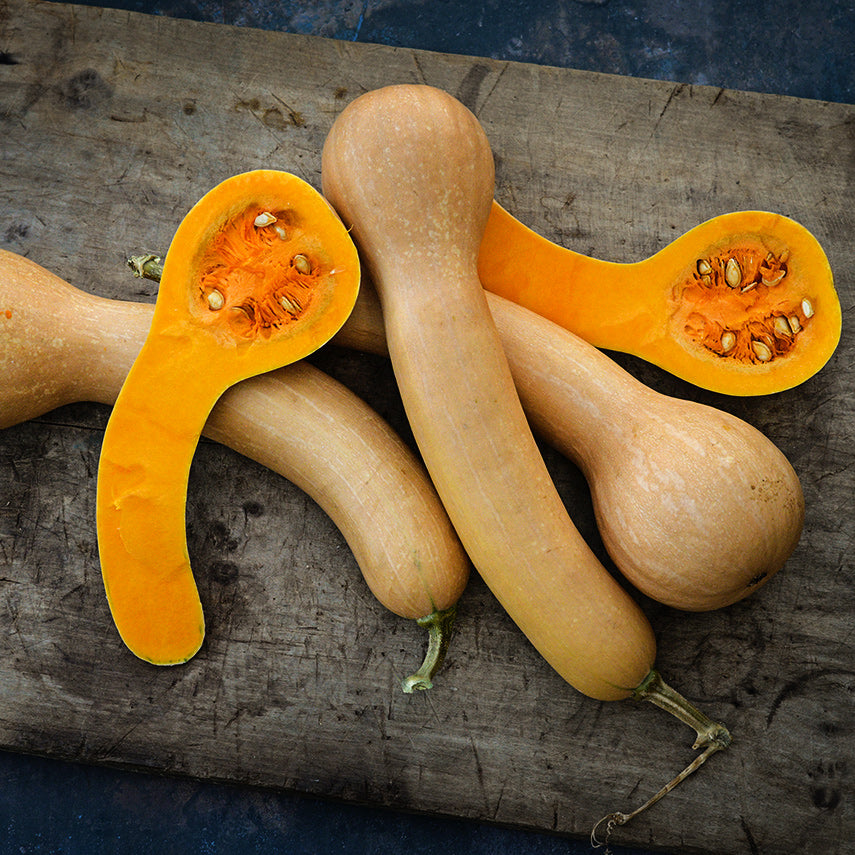 Halved and whole Canada Crookneck Winter Squash on a wood cutting board.