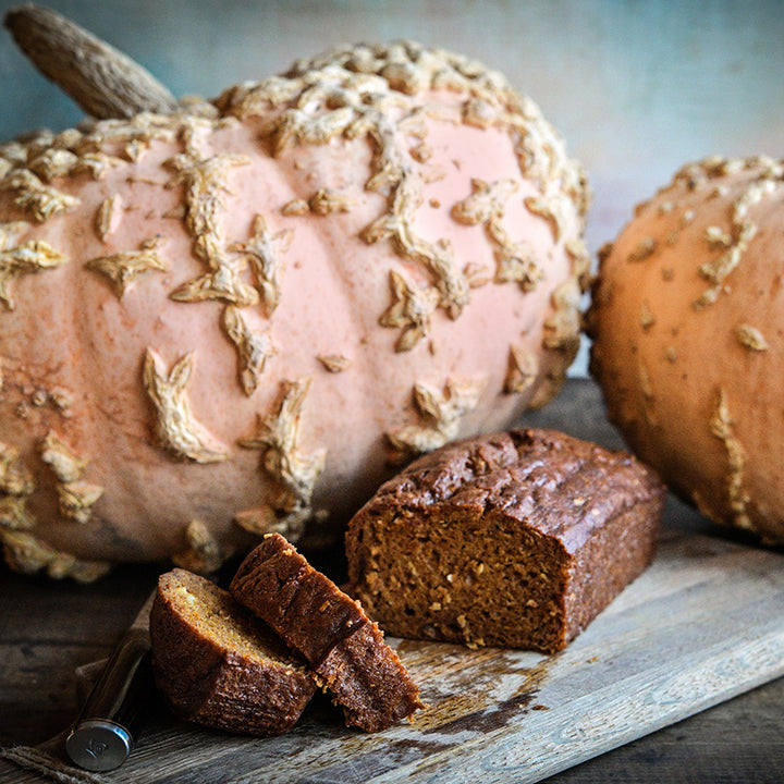 A loaf of sliced pumpkin bread on a wooden cutting board with knife and Galeux D&