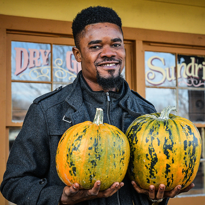 Man holding two Kakai Winter Squash in front of the Mercantile building at Baker Creek.