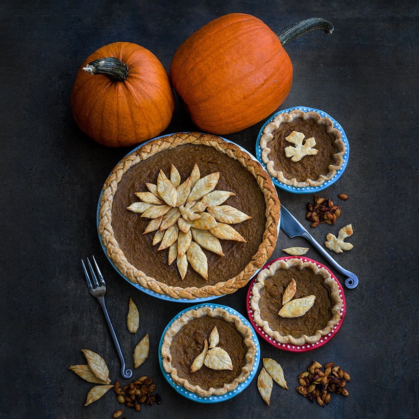 New England Sugar Pie Pumpkins with a quartet of pies and roasted seeds on a dark background.