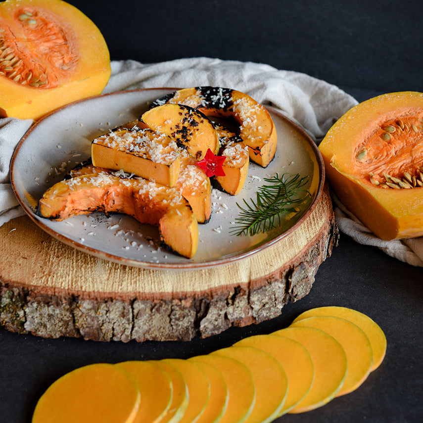 Roasted Butternut-Orange Winter Squash on a plate surrounded by cut squash on a dark background.
