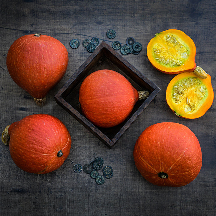 Whole and cut Red Kuri (Hokkaido) Winter Squash on a wood background with coins.