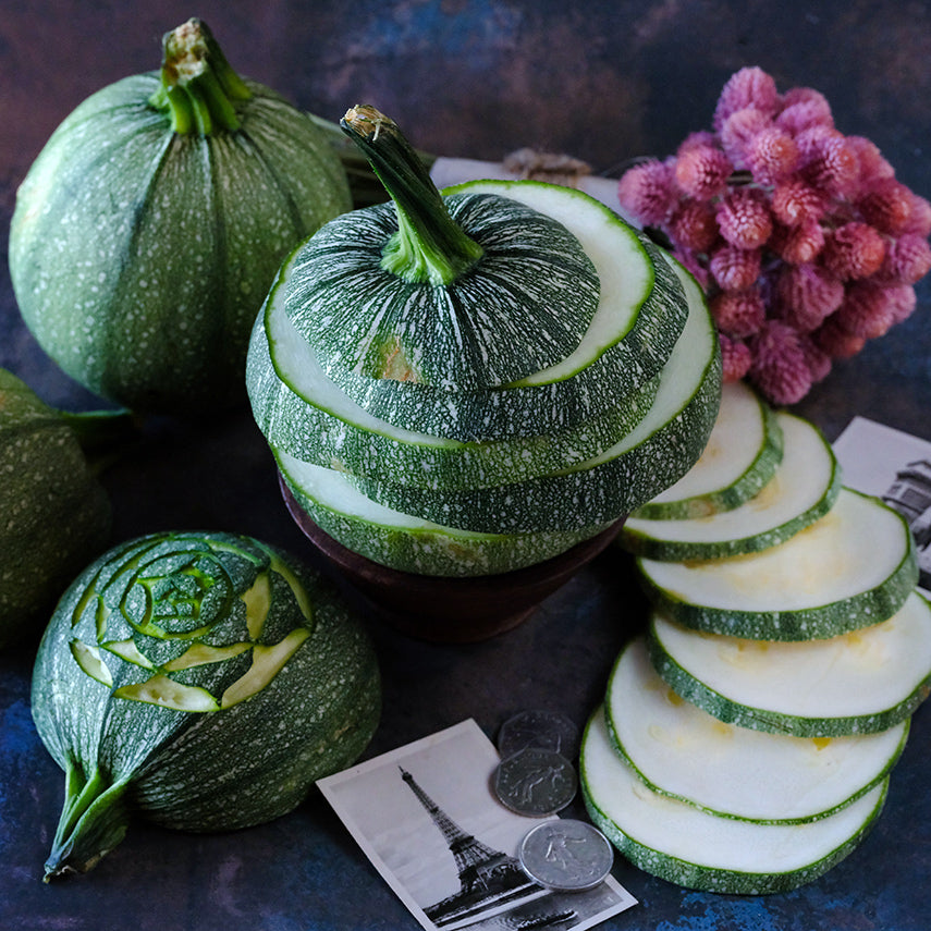 Sliced, cut and whole Ronde De Nice Summer Squash with postcards from France on a dark background.
