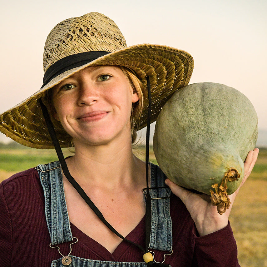 Baker Creek Manager holding a Sibley or Pikes Peak Winter Squash on her shoulder in the field.
